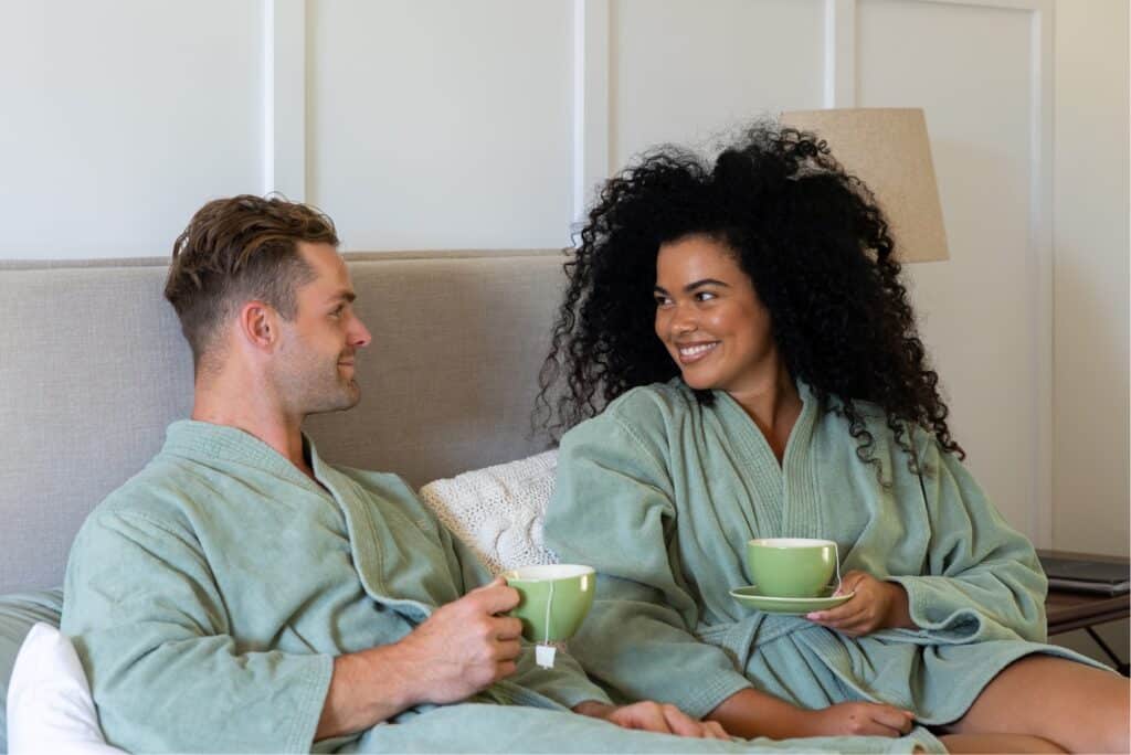 Man and woman dressed in Eden robes enjoy a cup of tea in bed at Eden Health Retreat